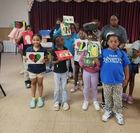 Children displaying colorful artwork in a room.