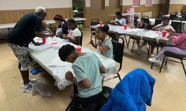 Children painting at tables in a classroom.