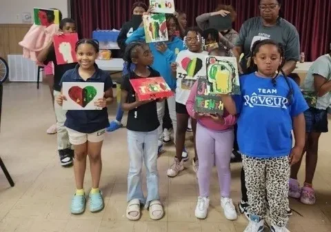 Children displaying colorful artwork in a room.